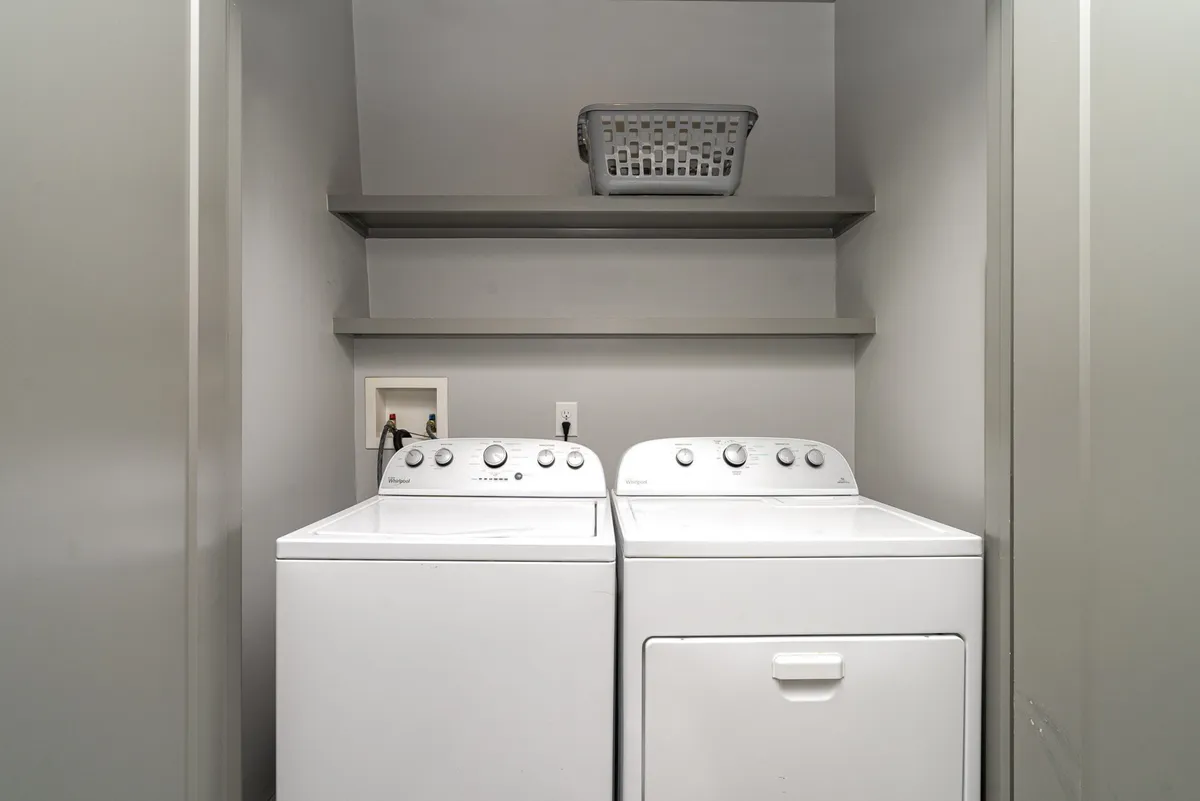 A practical laundry area equipped with a washer, dryer, storage shelf, and laundry basket. The space is organized and user-friendly, ideal for families or longer stays.
