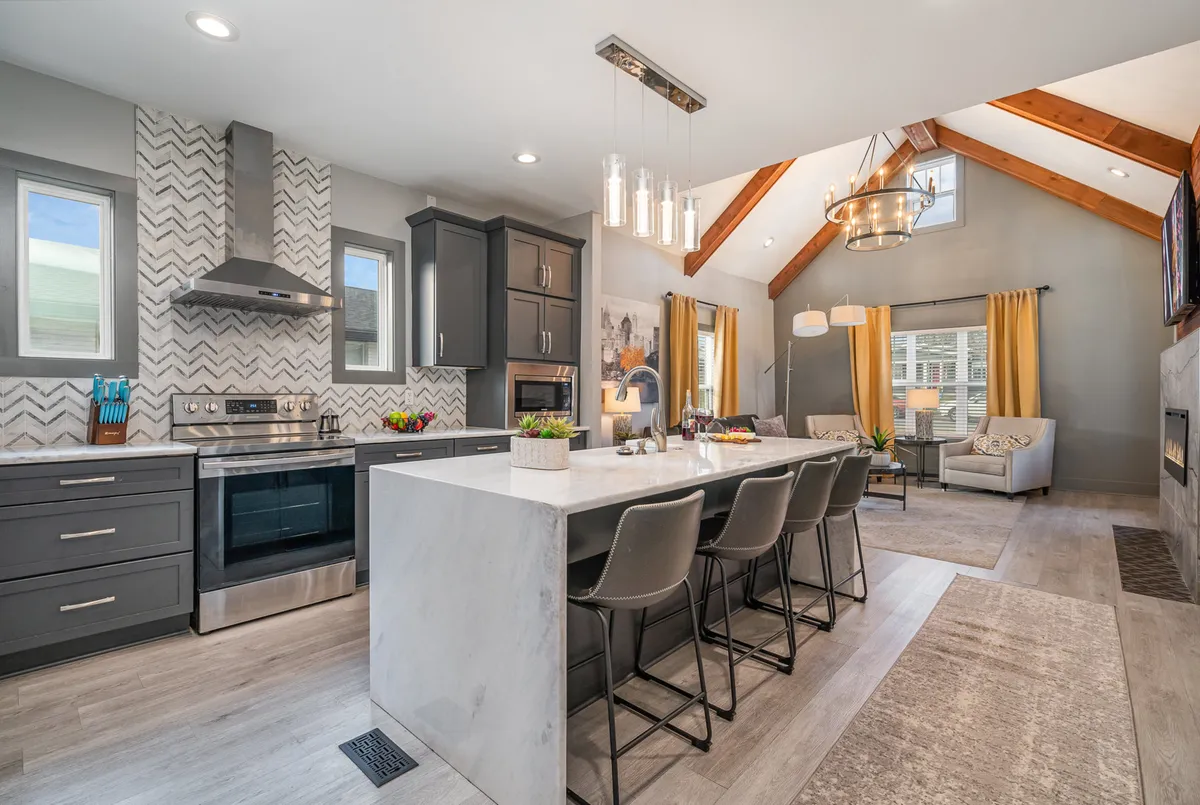 The image captures a warm, open-concept living space featuring a stunning marble kitchen island, a stylish chevron backsplash, bar stools set for conversation, and a comfortable living area complete with a cozy fireplace. The inviting layout is perfect for gatherings, cooking, and relaxing with friends or family.