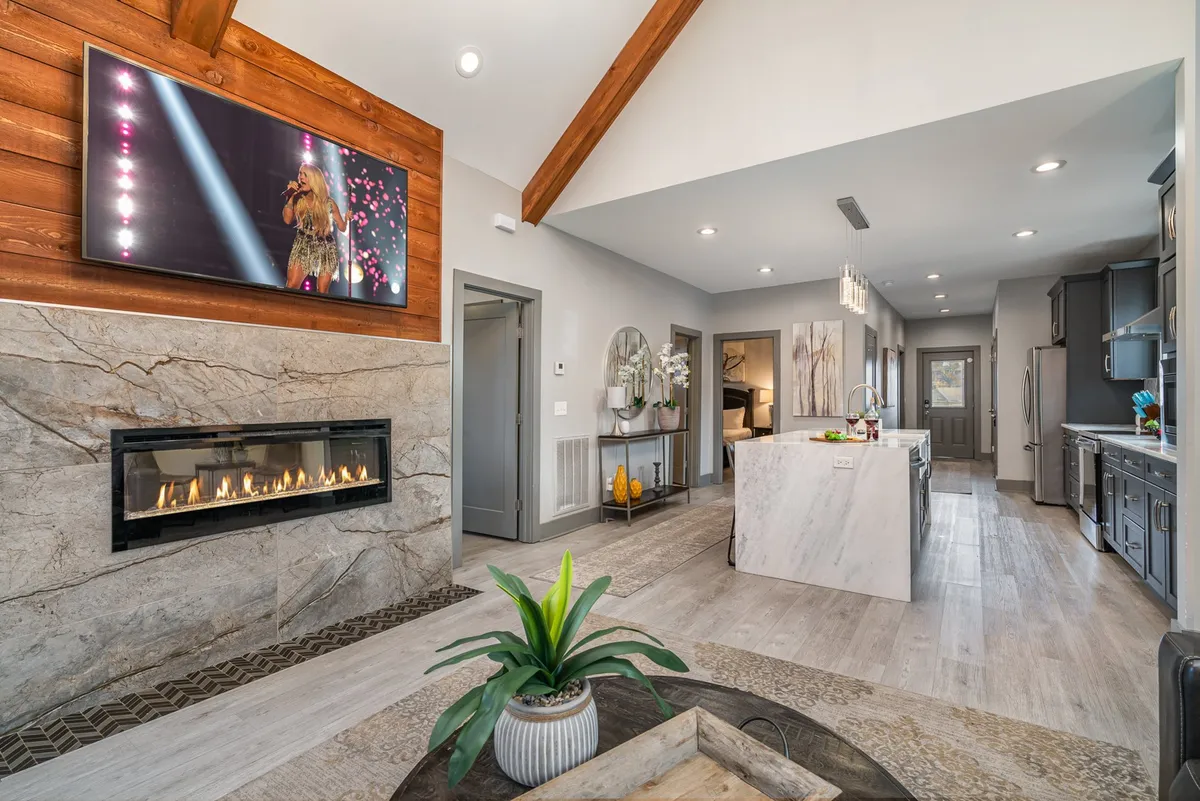An inviting view of the kitchen island adjoining the cozy living room, with a fireplace and television visible in the background. The island offers space for food prep or casual conversation, while the living space beckons for relaxation and entertainment.