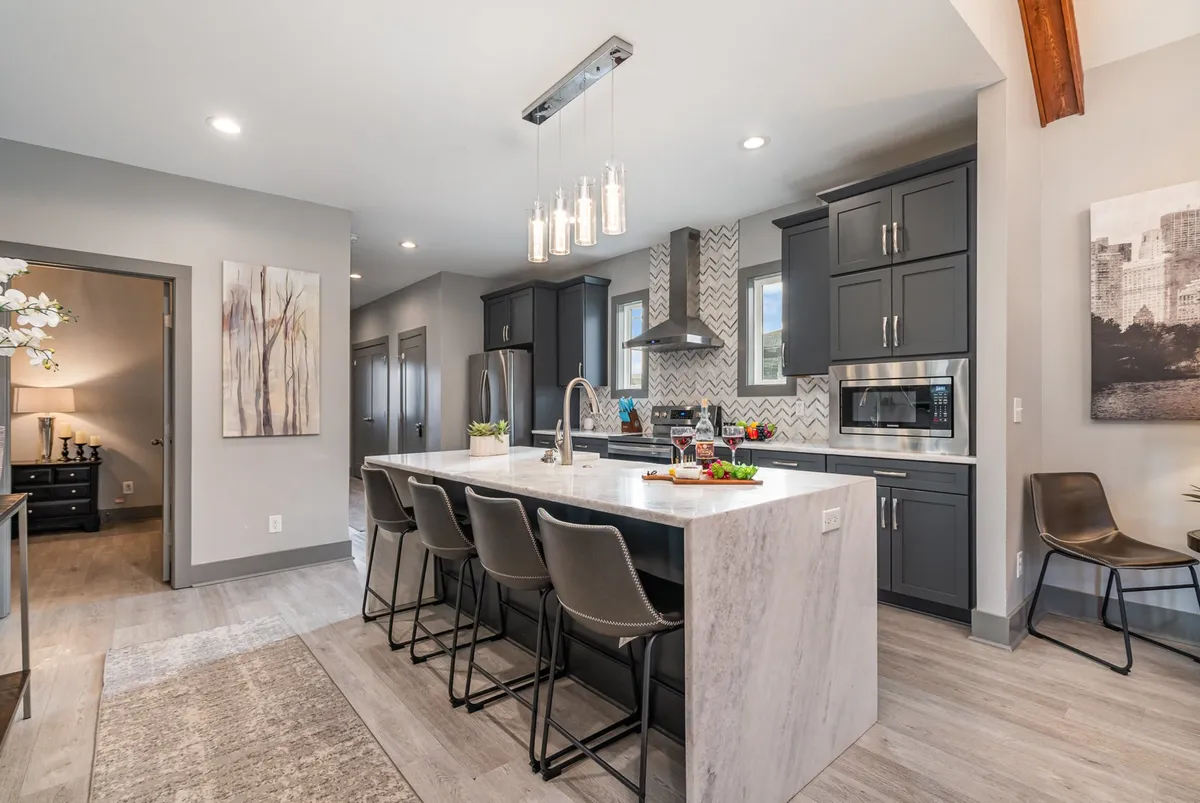 The image showcases a modern kitchen with a spacious island, sleek appliances, and warm decorative touches. The scene includes inviting lighting fixtures and comfortable seating, signaling a well-equipped space for preparing meals or gathering with family and friends.